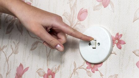 Eine Hand mit einem Lichtschalter. Licht wird ausgeschaltet.